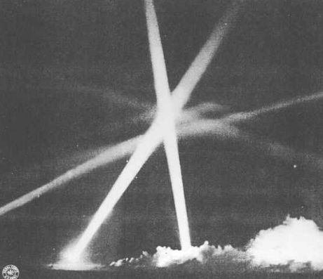 A German searchlight cone has a doomed bomber trapped.